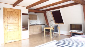 Un dormitorio con cama, escritorio, silla, televisión y una zona de cocina.