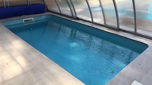 Una piscina interior con superficie de agua clara y azul, rodeada por un suelo de baldosas y una estructura de vidrio.