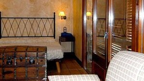 Habitación de hotel estrecha con una cama, una mesita pequeña y una silla. Hay un armario de madera y una ventana con persianas.