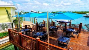 A wooden deck with tables and chairs, overlooking a body of water with boats. - Spanish Wells Yacht Haven (Spanish Wells)