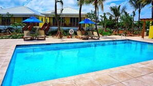 A swimming pool with lounge chairs and umbrellas, surrounded by palm trees and a building with a yellow facade. - Spanish Wells Yacht Haven (Spanish Wells)