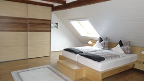 A bedroom with a sloped ceiling, a skylight, a bed with multiple pillows, a bedside table, and a wardrobe. - Apartment Panorama 2 near Airport (Elskop)
