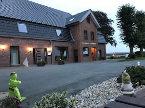 A brick building with a sloped roof and multiple windows, surrounded by a gravel driveway and small plants. - Apartment Panorama 2 near Airport (Elskop)