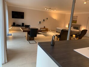 Una sala de estar moderna con comedor, un sofá, un sillón de masaje y un televisor montado en la pared.