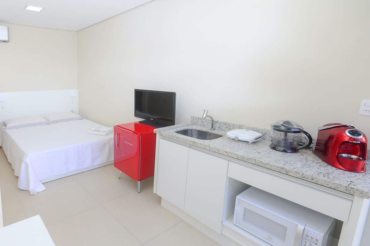 A small hotel room with a bed, a TV, a red refrigerator, a microwave, a coffee maker, and a sink.