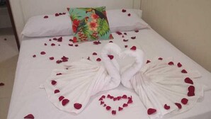 A bed with white linens, a floral pillow, and rose petals arranged in a heart shape and a swan design.