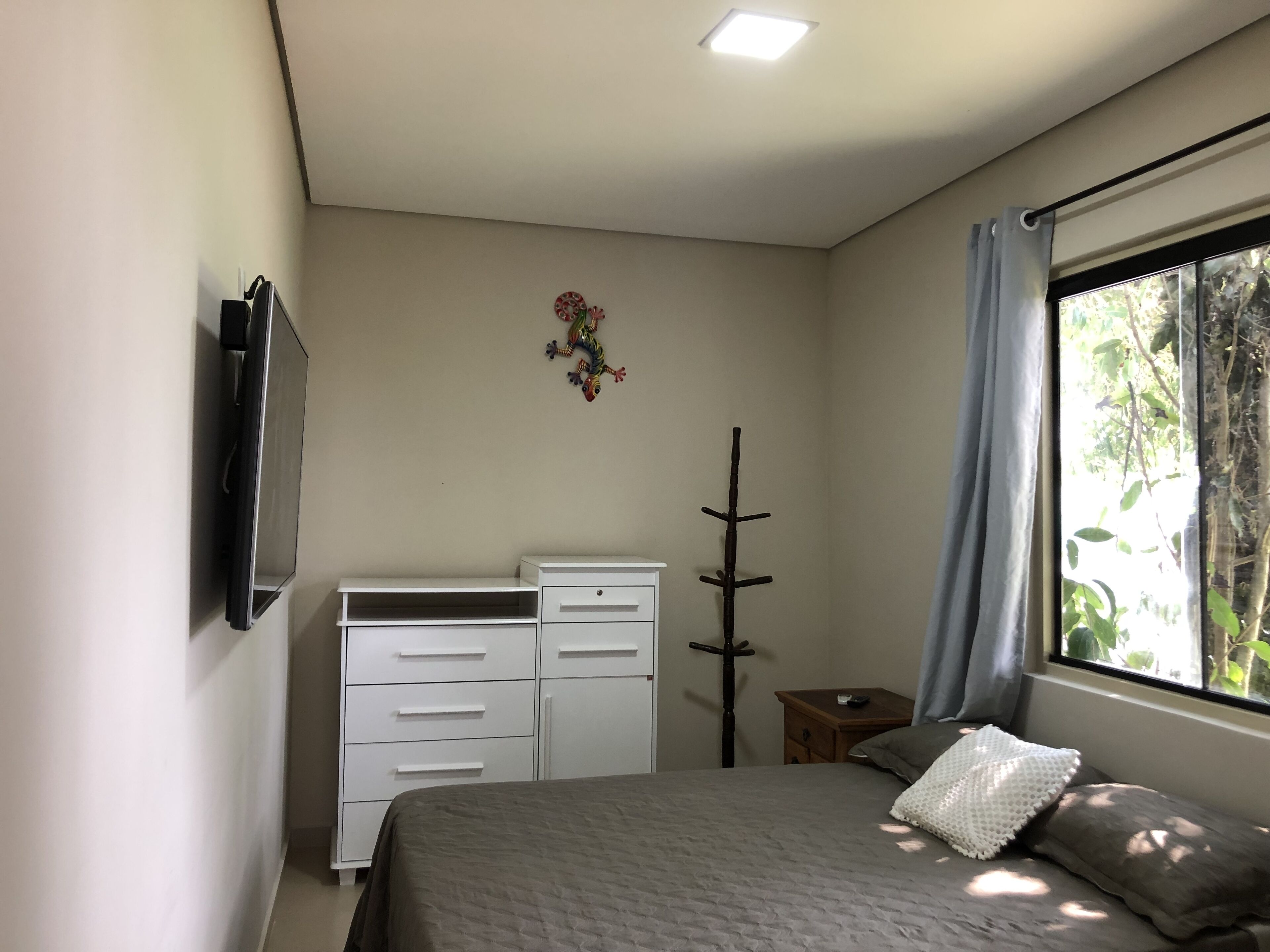 A bedroom with a bed, a dresser, a coat rack, a TV, and a window with curtains.