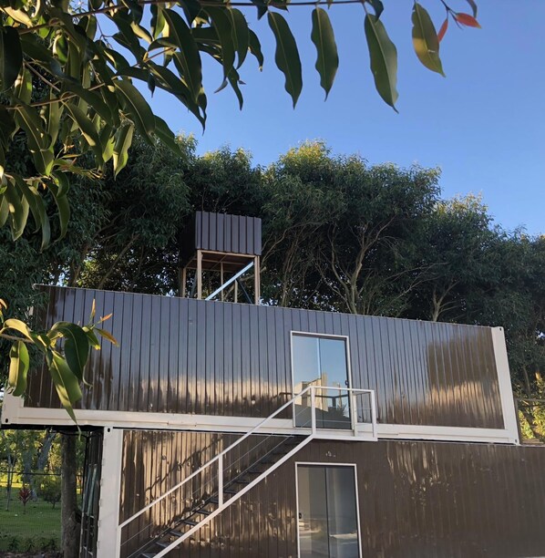Un edificio moderno de dos pisos con fachada metálica y puerta de vidrio en la parte inferior.