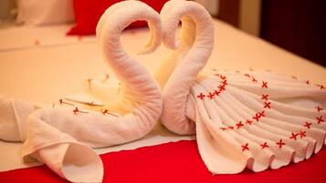 Een bed met witte handdoeken gevouwen in de vorm van zwanen, een rood kussen en een witte dekbedovertrek.