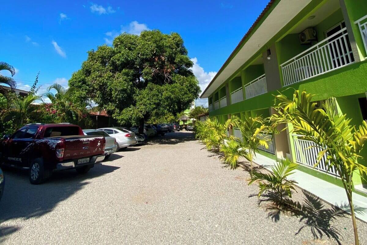 A green building with a satellite dish, parked cars, and a large tree in front.