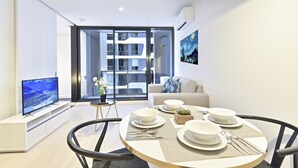 Una sala moderna con un televisor de pantalla plana, una mesa de comedor con platos y cubiertos, un sofá y un amplio ventanal con vista a un edificio.