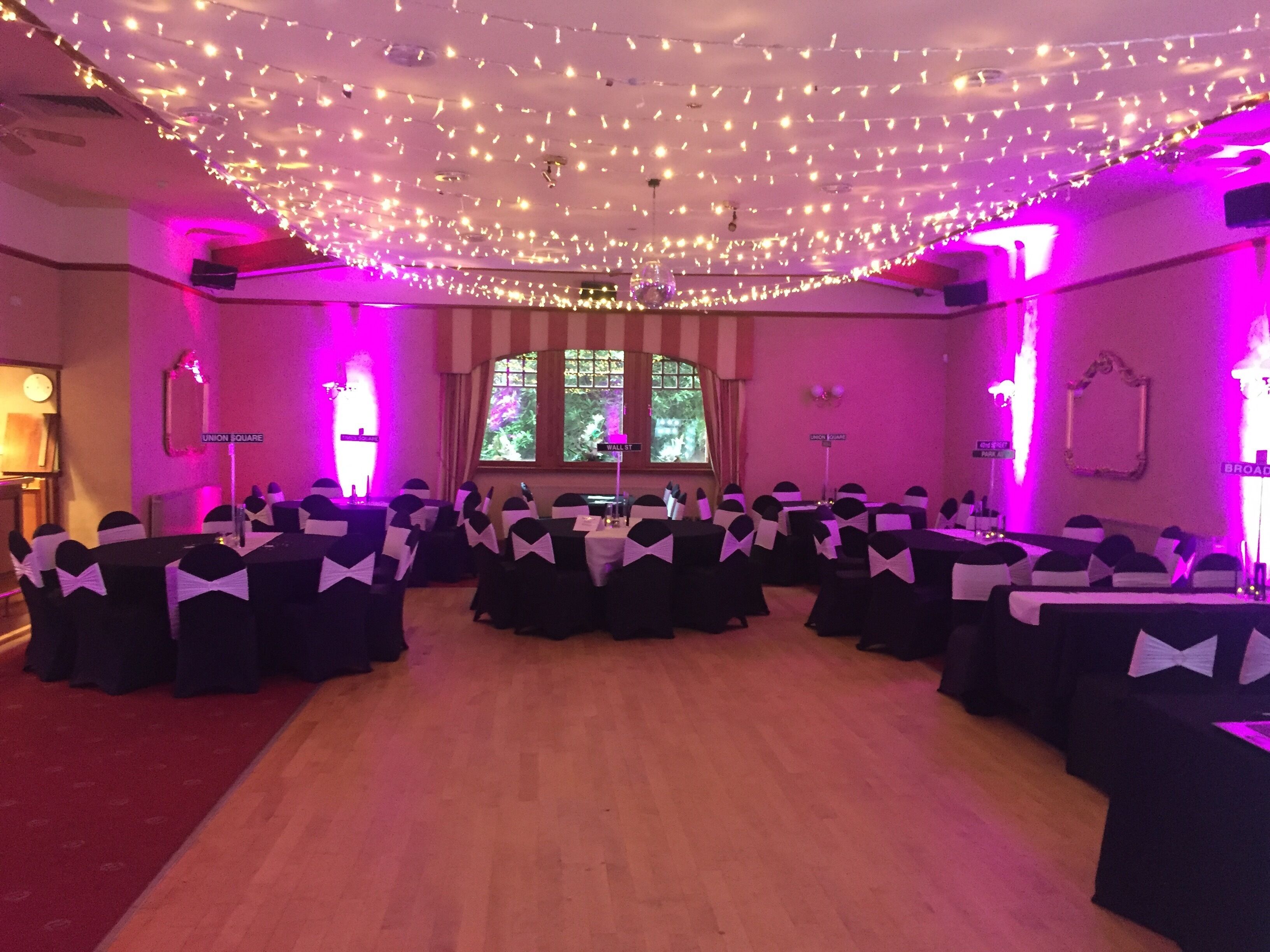 Een feestzaal met tafels in een halve cirkel, versierd met zwart-witte tafellakens en stoelen met witte linten.
