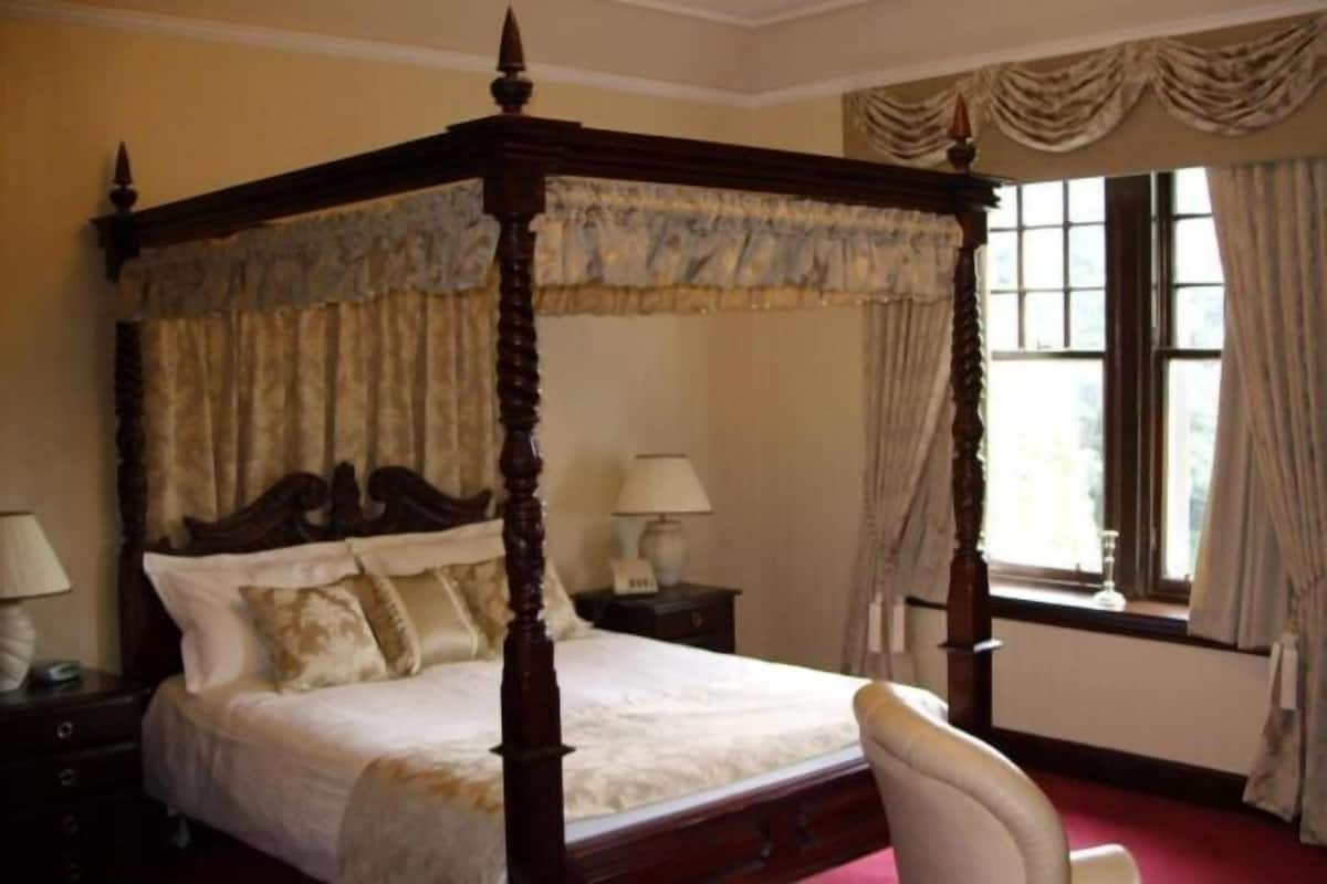 A four-poster bed with a canopy, a nightstand with a lamp, and a window with curtains.