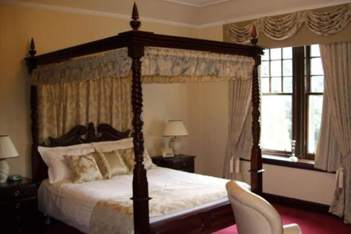 A four-poster bed with a canopy, a nightstand with a lamp, and a window with curtains.