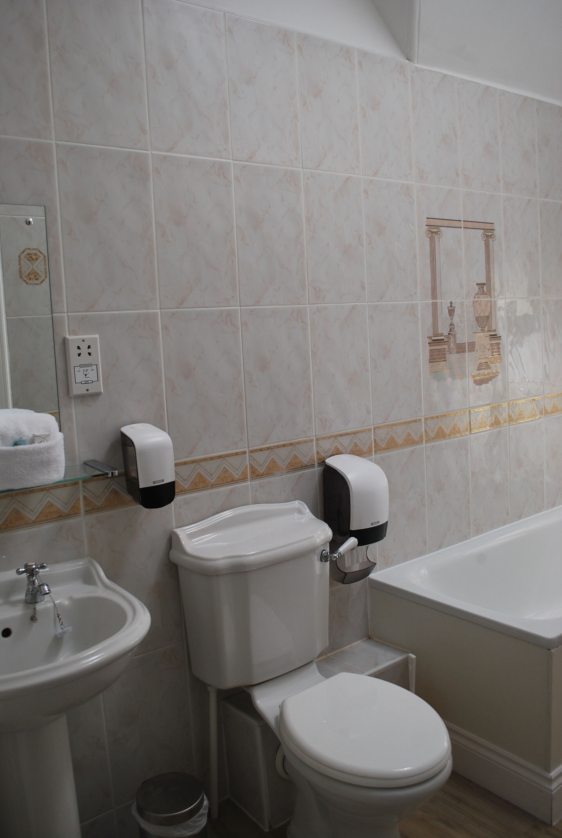 A bathroom with a toilet, sink, and bathtub. There are two soap dispensers on the wall.