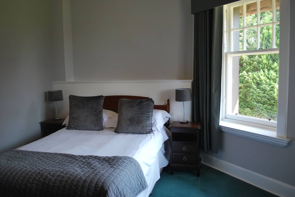 A neatly made bed with a grey quilt, two bedside tables with lamps, and a window with curtains.