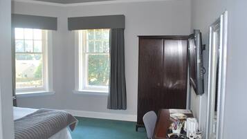 A bedroom with a bed, a desk, a chair, a wardrobe, and two windows with curtains.