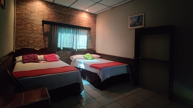 Een hotelkamer met twee bedden, een raam met gordijnen, een houten wand en een klein kastje.