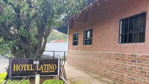 Een bord met de tekst 'Hotel Latino', met op de achtergrond een gebouw van baksteen en een boom.