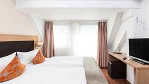 A hotel room with a bed, two pillows, a desk with a TV, and a window with curtains. - Hotel Sarah (Heinsberg)