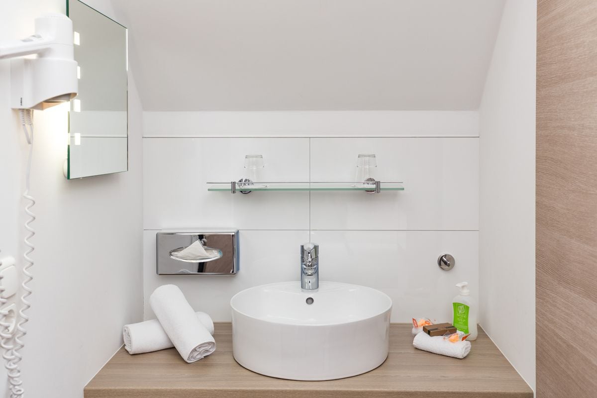 A modern bathroom with a round sink, a glass shelf above the sink, a mirror, and a towel dispenser.