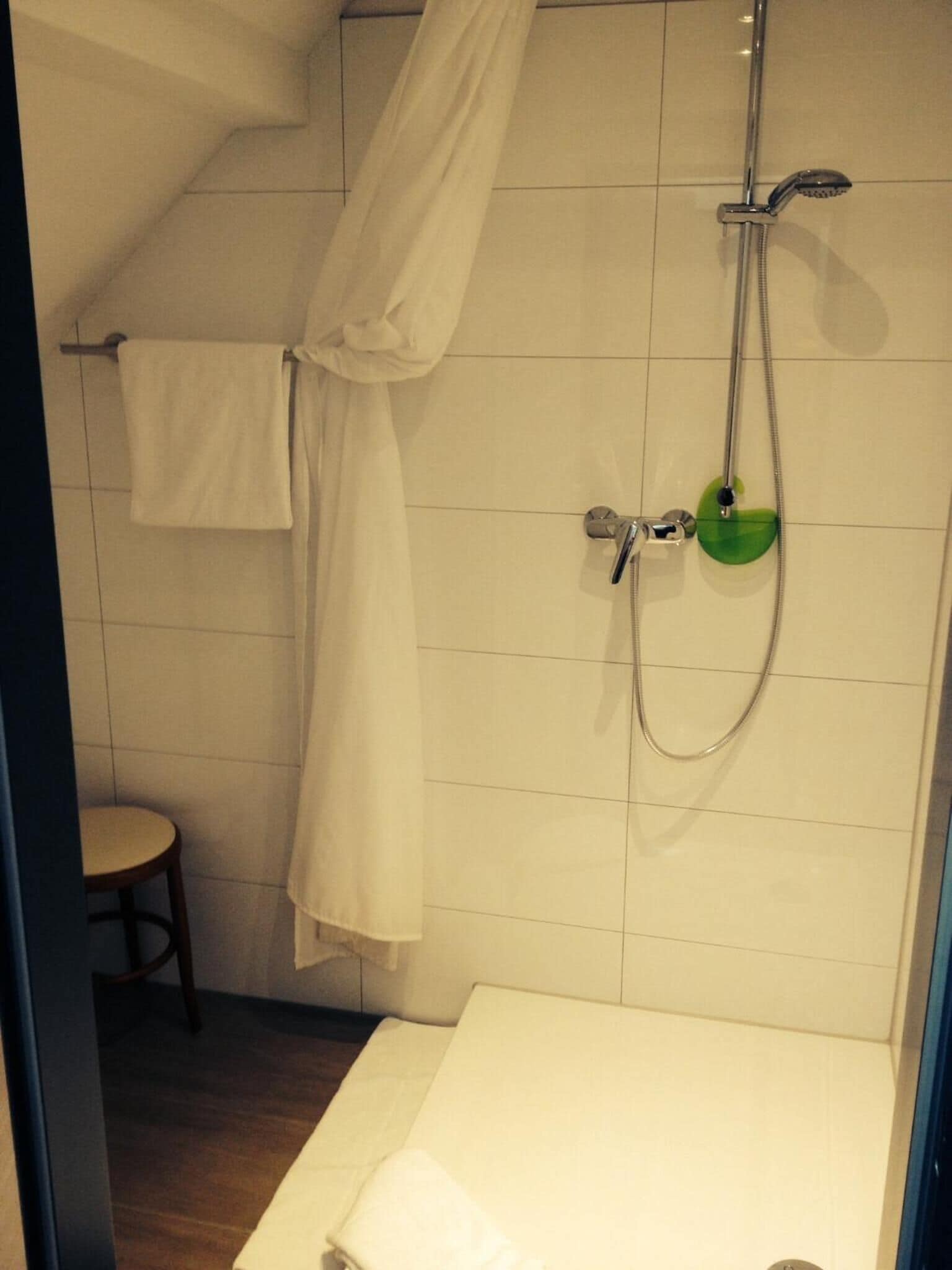 Un baño con ducha, perchero y un taburete pequeño.