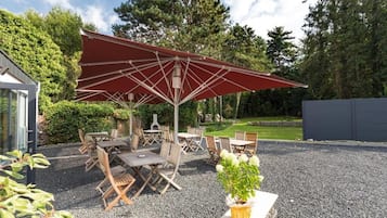 An outdoor patio with a red umbrella, wooden tables and chairs, and a gravel ground.