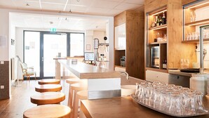 A modern bar area with a wooden counter, stools, and a tray of glasses. - Hotel Sarah (Heinsberg)