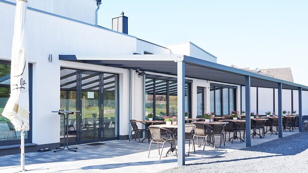 A modern outdoor seating area with tables and chairs, large glass windows, and a covered patio. - Hotel Sarah (Heinsberg)