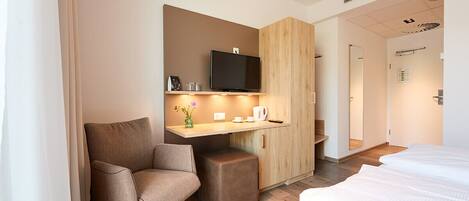 Una habitación de hotel moderna con cama, escritorio con televisor, una silla y un pequeño armario.