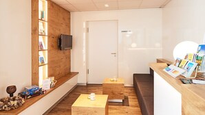 A reception area with a wooden bookshelf, a flat-screen TV, a reception desk with brochures, and a door labeled "ZIMMER 1 - 11". - Hotel Sarah (Heinsberg)