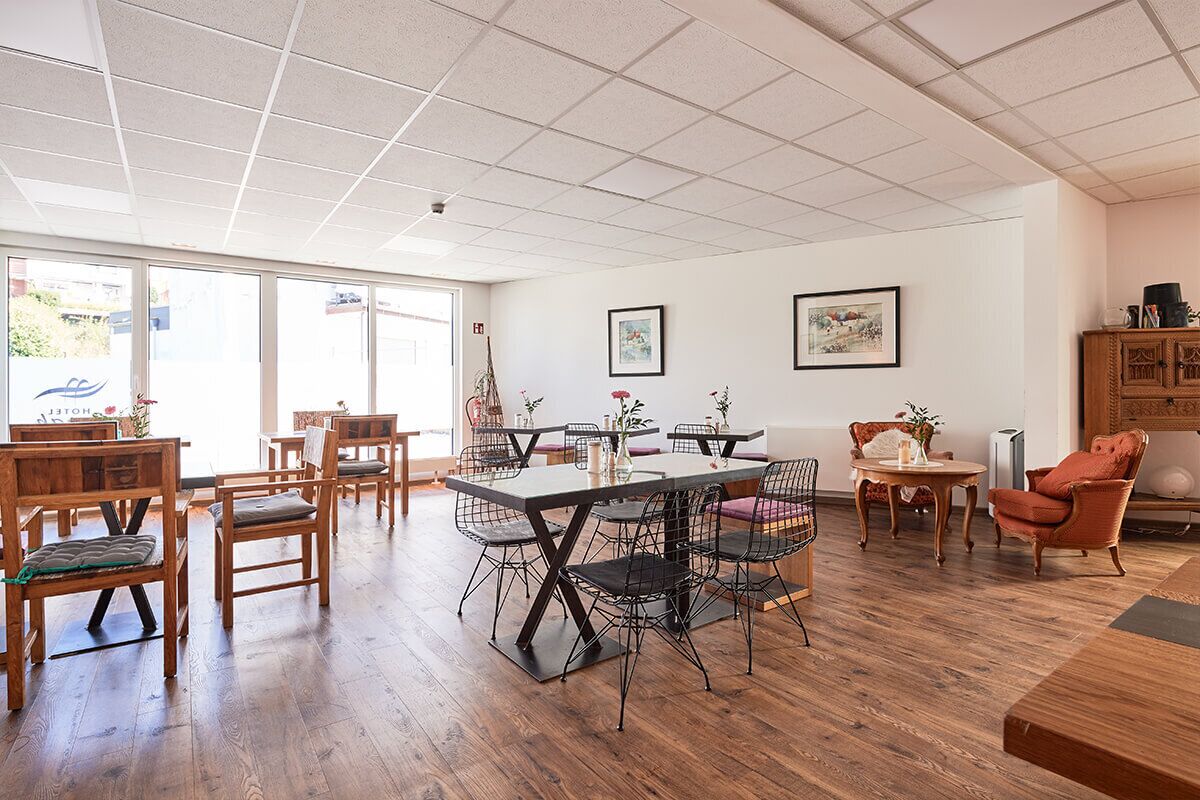 Un comedor amplio con mesas y sillas de madera, un ventanal con vistas y un aparador con objetos decorativos.