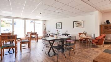 Un comedor amplio con mesas y sillas de madera, un ventanal con vistas y un aparador con objetos decorativos.