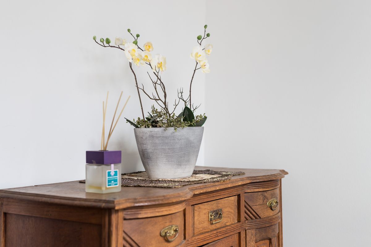 A wooden dresser with a potted orchid and a reed diffuser.