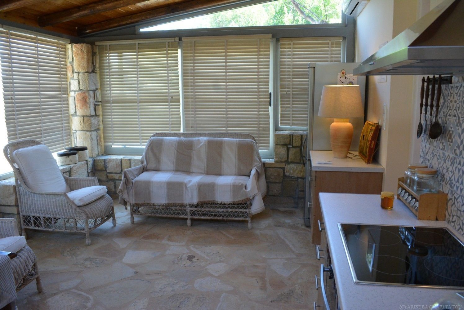 Un espace patio accueillant avec un canapé et des fauteuils en osier, un sol en pierre et une cuisine équipée d’une cuisinière et de bocaux.