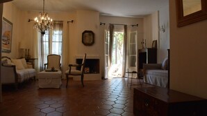 Un salón espacioso con suelo de baldosas hexagonales, una araña, chimenea y un gran ventanal con cortinas.