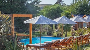 A pool area with wooden lounge chairs and umbrellas, surrounded by greenery and a wooden fence. - Balcon del Golf Resort, Spa & Restaurant. (Sierra de la Ventana)