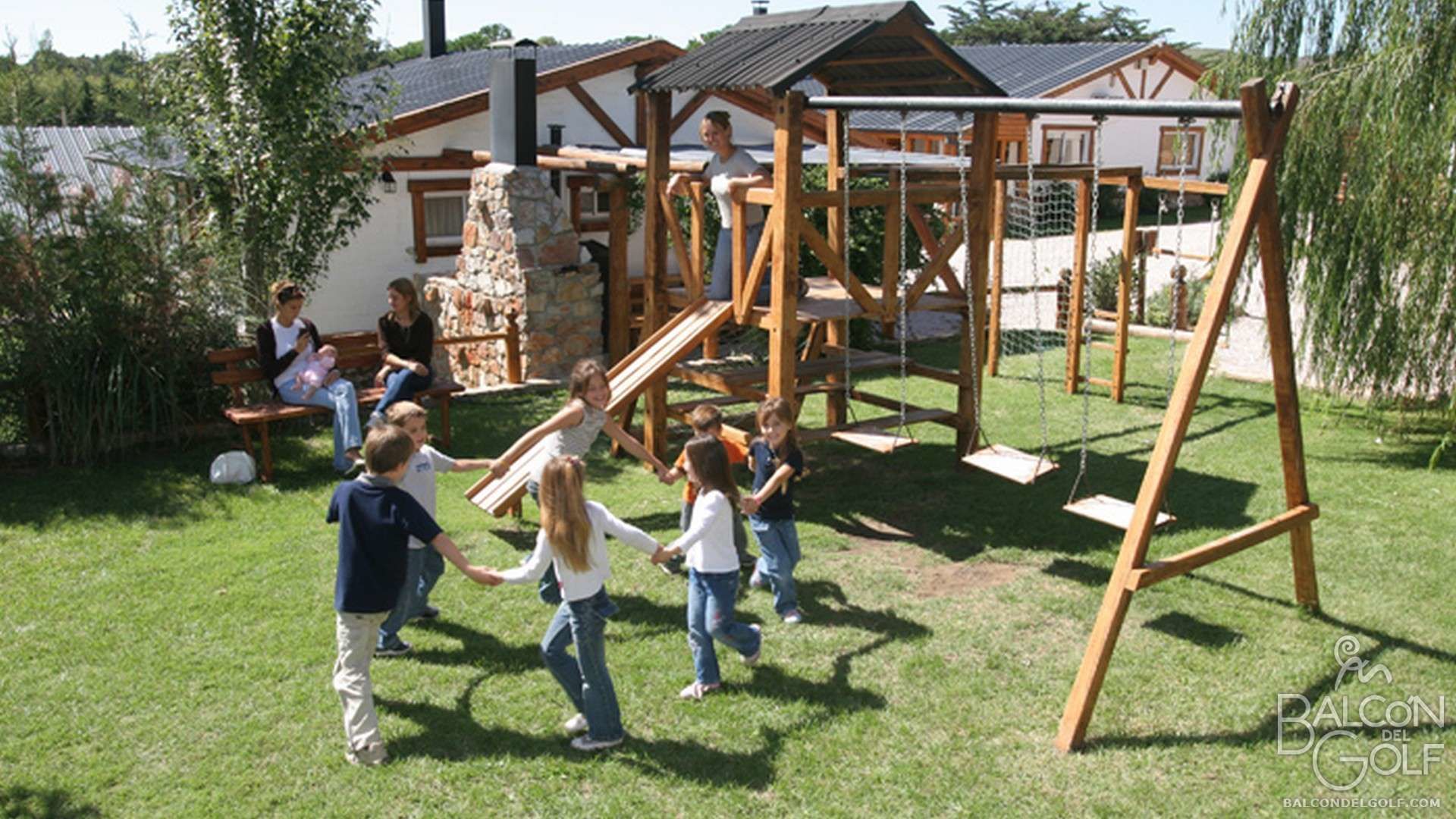 Una estructura de juego de madera en un patio cubierto de césped, con una casa al fondo.