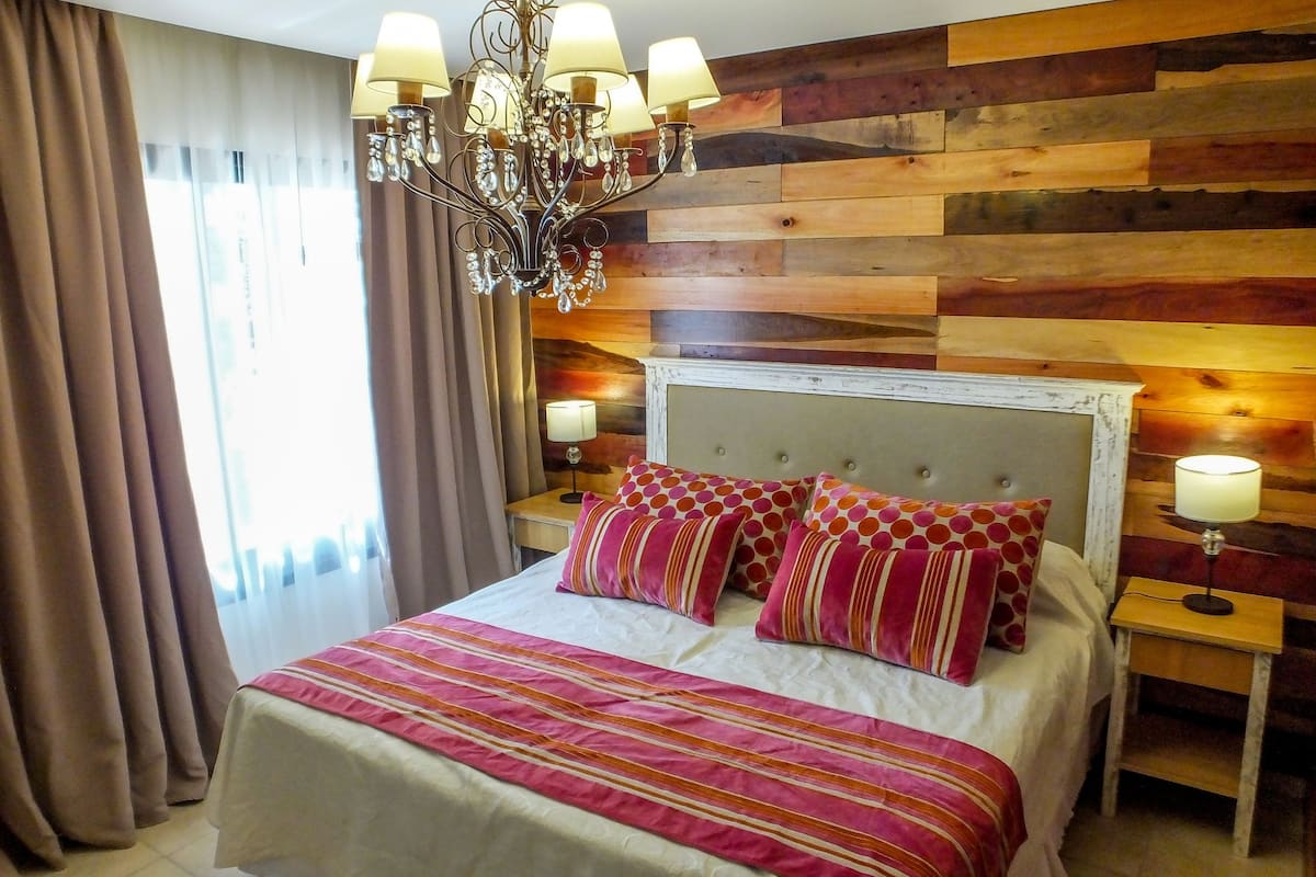 Une chambre à coucher avec un lit, un lustre, des murs lambrissés, des rideaux et des lampes de chevet.