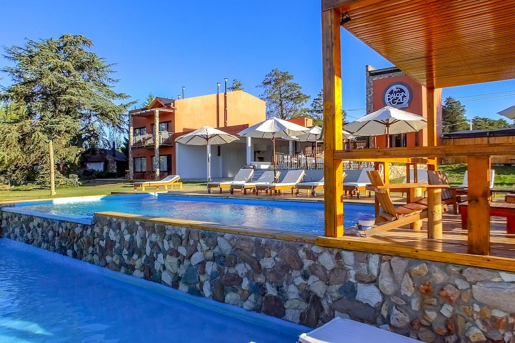 A pool area with lounge chairs and umbrellas, a stone wall, and a building with a sign that reads "Balcon Golf".