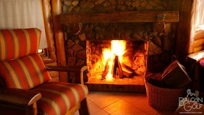 A cozy room with a stone fireplace, a striped armchair, and a wicker basket. - Balcon del Golf Resort, Spa & Restaurant. (Sierra de la Ventana)