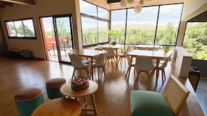 A spacious room with wooden floors, a high ceiling, and large windows offering a view of greenery. There are several tables and chairs arranged for dining or socializing. - Balcon del Golf Resort, Spa & Restaurant. (Sierra de la Ventana)