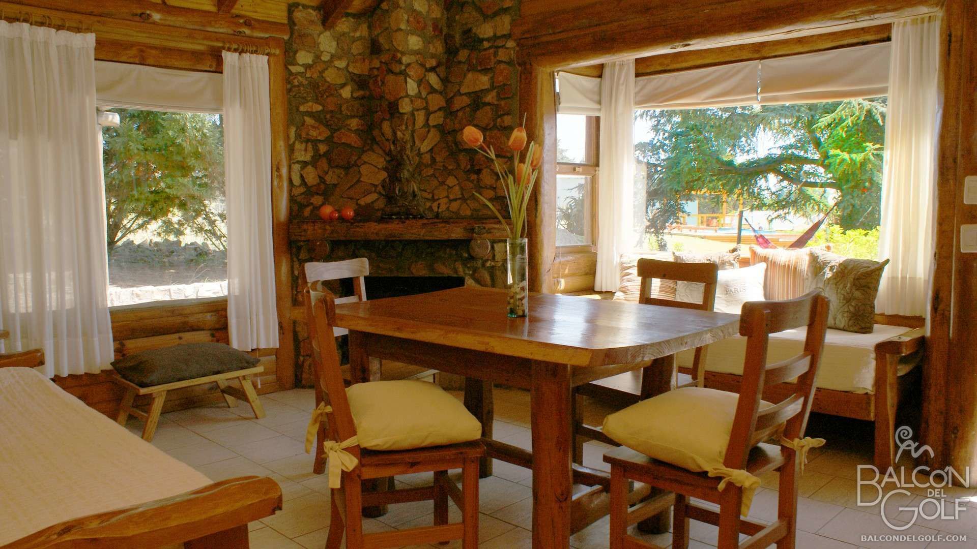 A wooden dining area with a stone wall, a table, chairs, and a view of the outdoors.