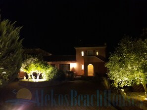Une vue nocturne d’un bâtiment dont l’entrée est bien éclairée et qui est entouré de verdure.