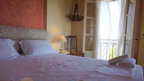 A neatly made bed with a pink bedspread and pillows, a bedside lamp, and a wooden chair. - Alekos Beach Houses - Natura Gialla (Kefalonia)