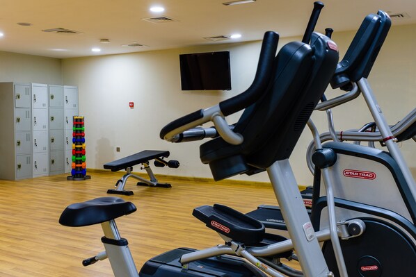 Un gimnasio con bicicletas estáticas, una banca y un televisor en la pared.