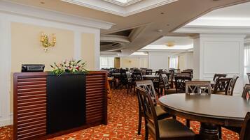 A hotel lobby with a reception desk, multiple dining tables, and chairs.
