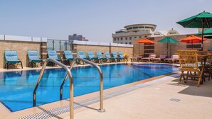 Ein Dachpool mit Liegestühlen und Sonnenschirmen, umgeben von einem Hochhaus.