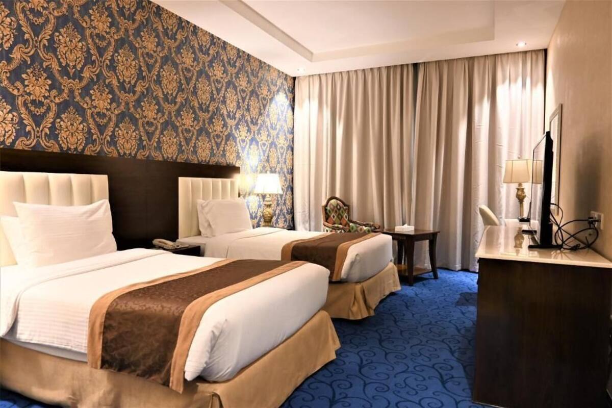 Habitación de hotel con dos camas, un escritorio, una silla, un espejo y un televisor.