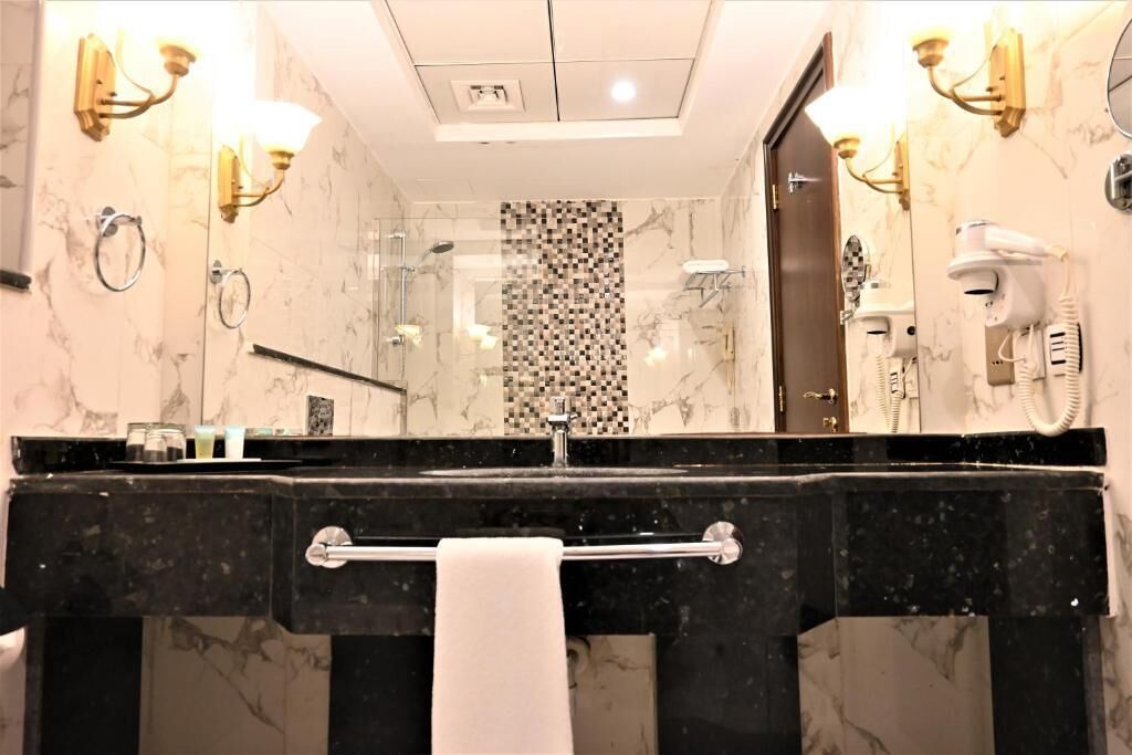 A modern bathroom with a marble vanity, a towel rack, a glass shower enclosure, and a hairdryer mounted on the wall.